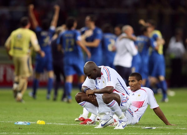 世界杯FIFA体育新闻：在2006年德国世界杯决赛中，法国球员阿利乌·迪亚拉和弗洛伦特·马卢达在柏林奥林匹克体育场点球大战失利后，眼睁睁地看着意大利球员在他们身后庆祝，脸上露出沮丧的神情。