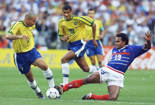 世界杯FIFA体育新闻：1998年7月12日，在圣丹尼斯法兰西体育场举行的世界杯决赛中，法国球员克里斯蒂安·卡伦布（右）受到巴西球员罗纳尔多（左）和里瓦尔多的拼抢。上半场结束时，法国队以2-0领先。（电子图片）法新社/帕特里克·赫尔佐格摄（图片由帕特里克·赫尔佐格/法新社通过盖蒂图片社提供）