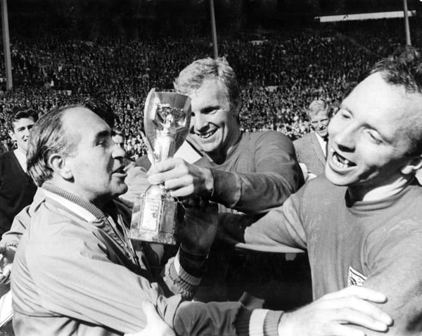 世界杯FIFA体育新闻:1966年世界杯,英格兰队主教练阿尔夫·拉姆齐正要亲吻英格兰队长博比手中的雷米特杯。